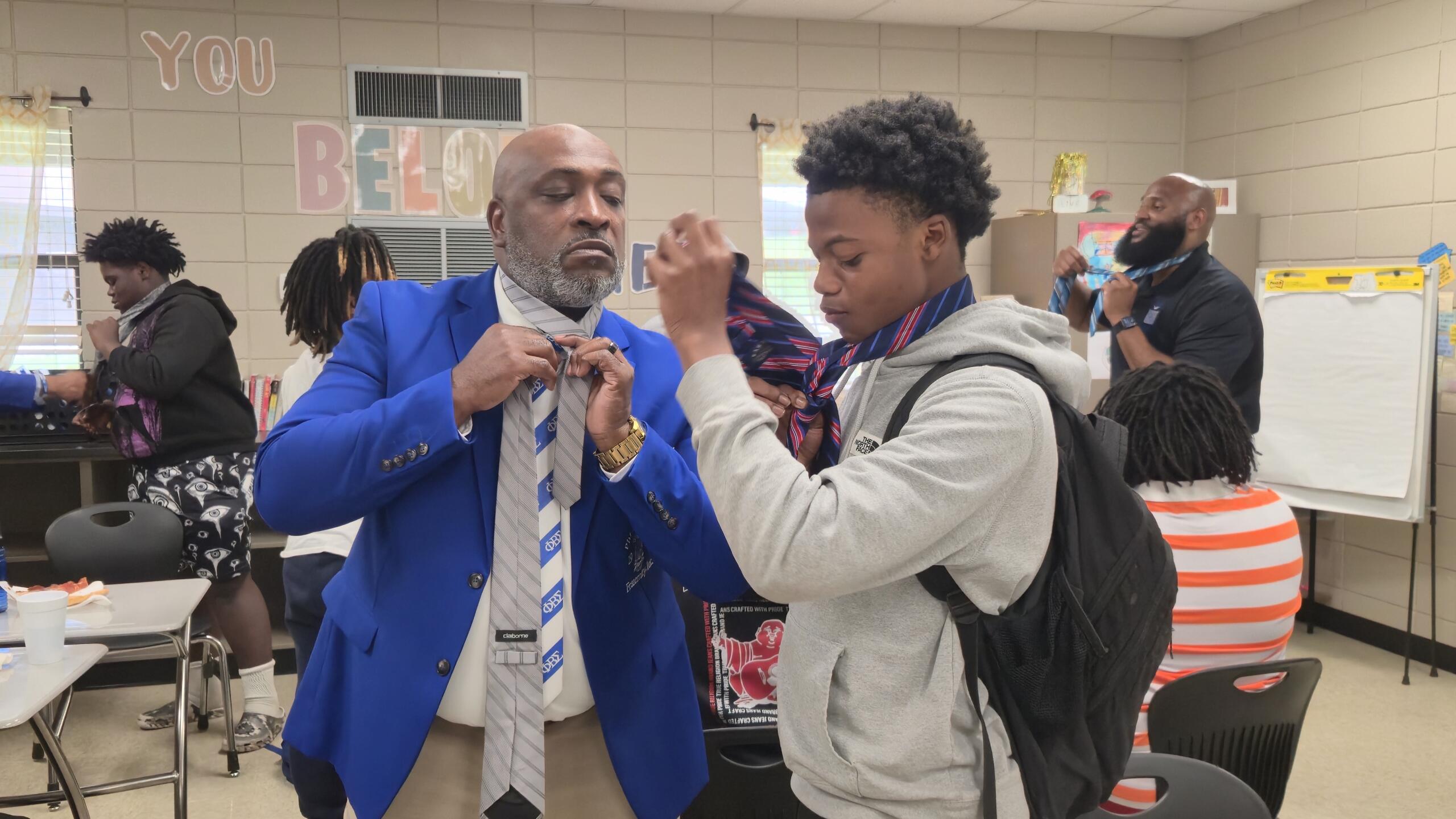 A fraternity member works with a student on tying his necktie