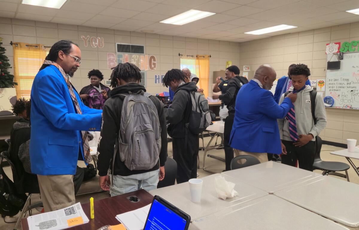 Fraternity members teach students at Douglas MacArthur Junior High School how to tie a necktie.