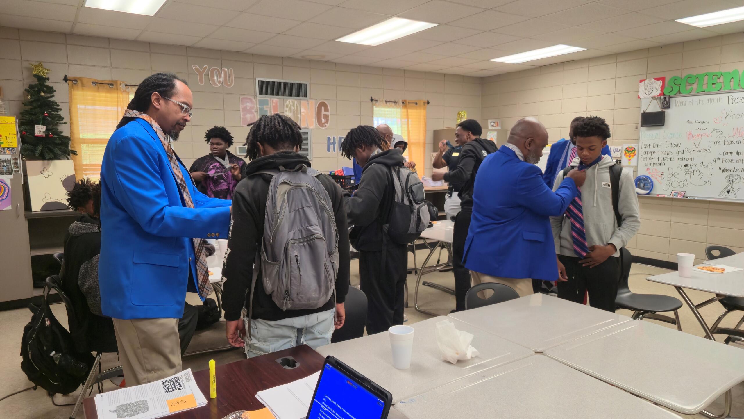 Fraternity members teach students at Douglas MacArthur Junior High School how to tie a necktie.