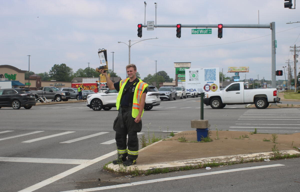 Jonesboro Fire Department Rookie Hunter Pagan poses with the boot on the intersection of Red Wolf Boulevard and Nettleton Avenue.