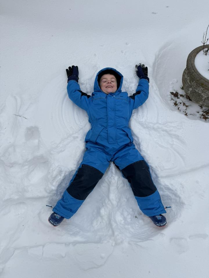 boy in blue snow gear making a snow angel