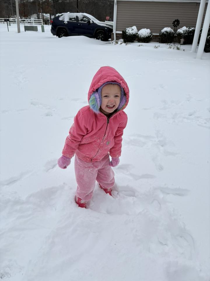 a little girl with a pink outfit and ear muffs in the snow