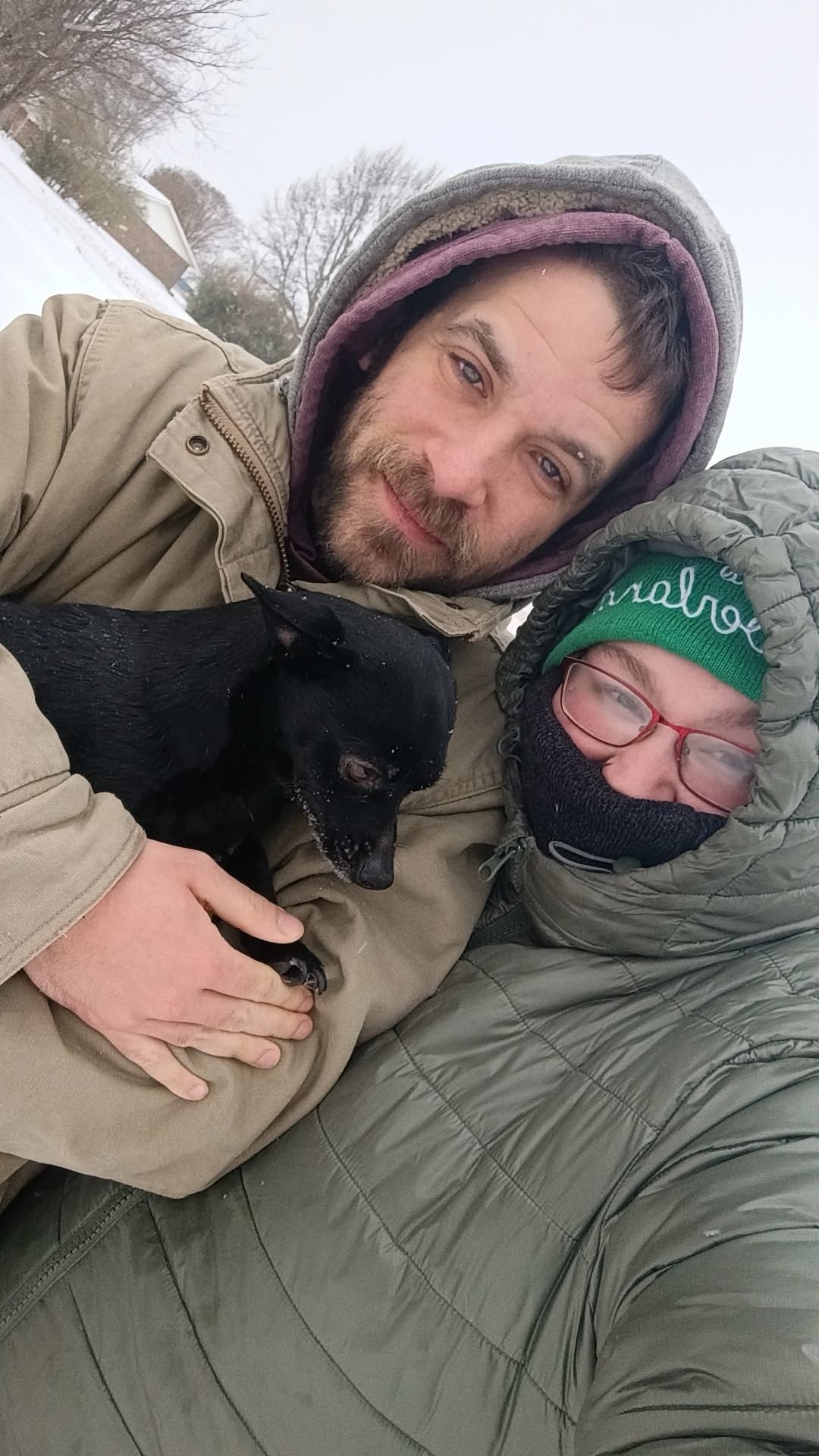 two people holding a small black dog in the snow