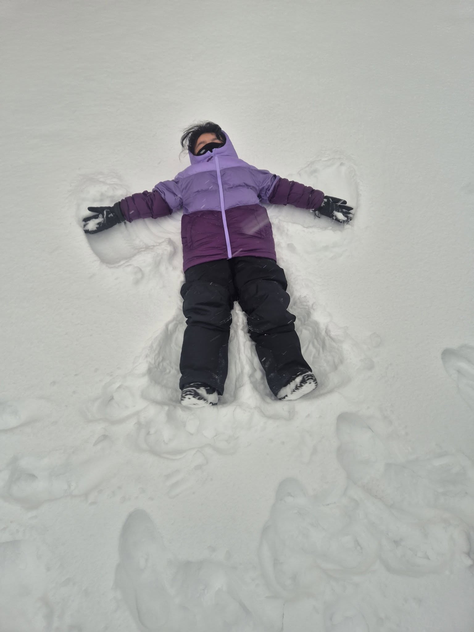 child making a snow angel with purple jacket