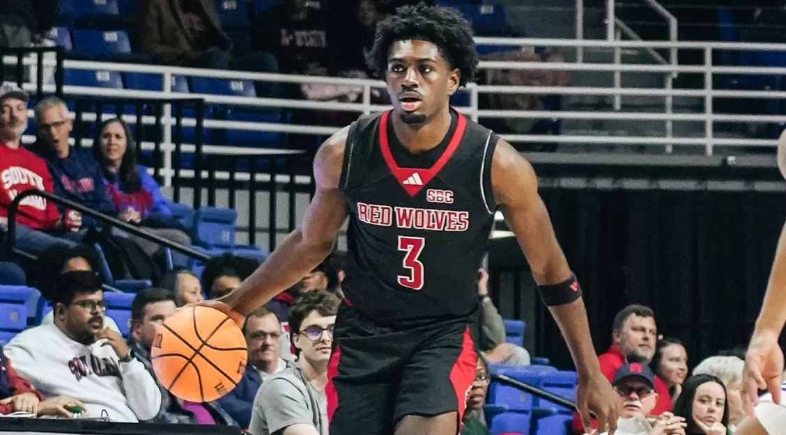 black man with basketball in Red Wolves jersey on court action shot