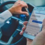 man holds cell phone and steering wheel while driving