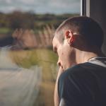 young man looks out window with hand on head