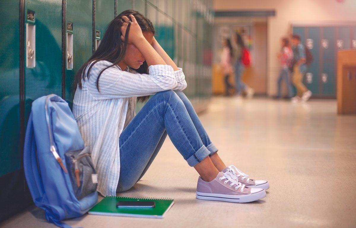 student puts her head in her hands while sitting against lockers