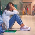 student puts her head in her hands while sitting against lockers