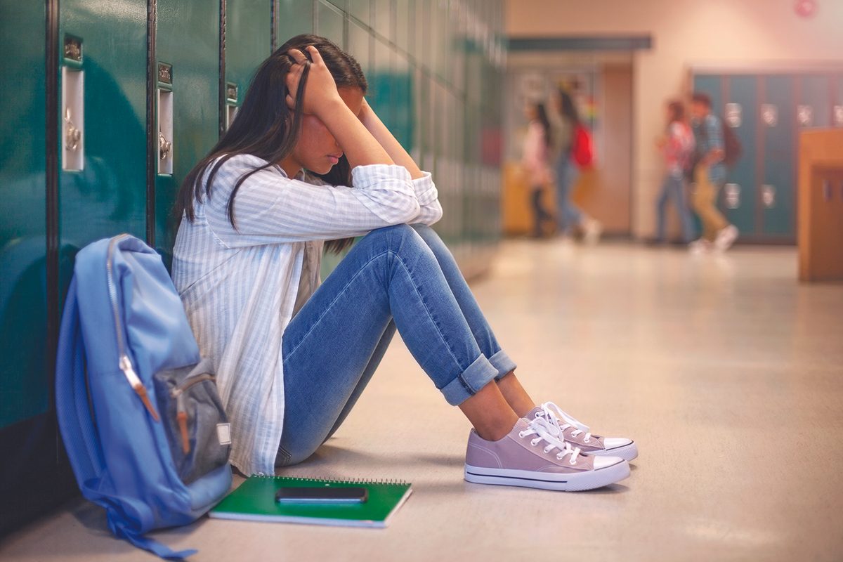 student puts her head in her hands while sitting against lockers