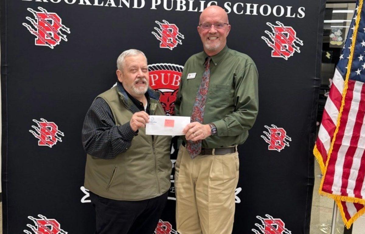 two men stand in front of step and repeat holding a check