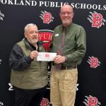 two men stand in front of step and repeat holding a check