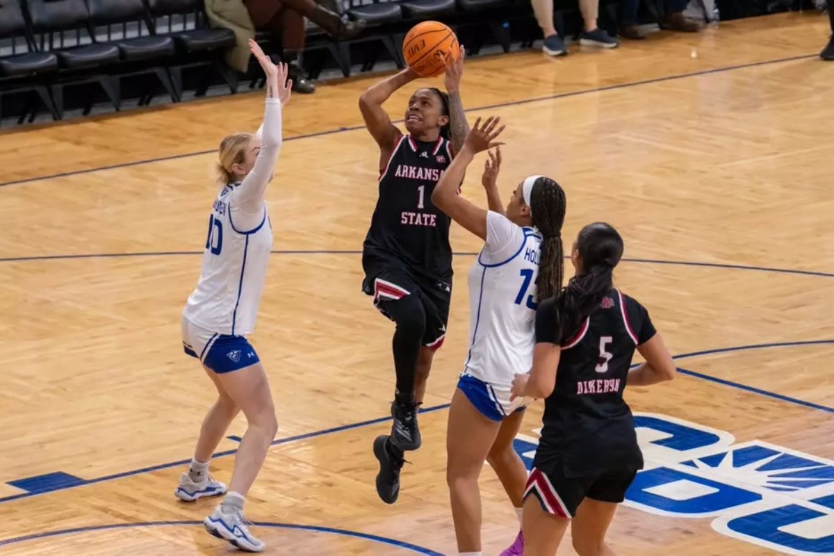 four basketball players two in black A-State jerseys two in white jerseys on court one player is shooting