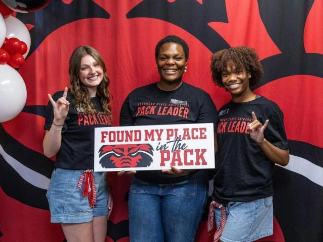 Three A-State Pack Leaders smile and pose with a “Found My Place in the Pack” sign.