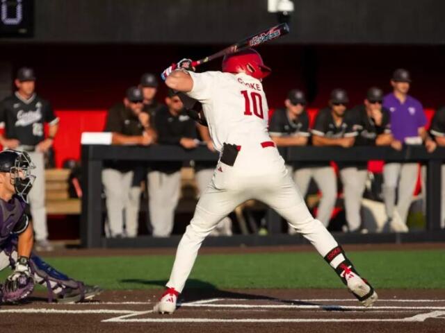 Baseball batter in a white uniform with number 10 swings at a pitch near home plate, catcher crouched behind him.