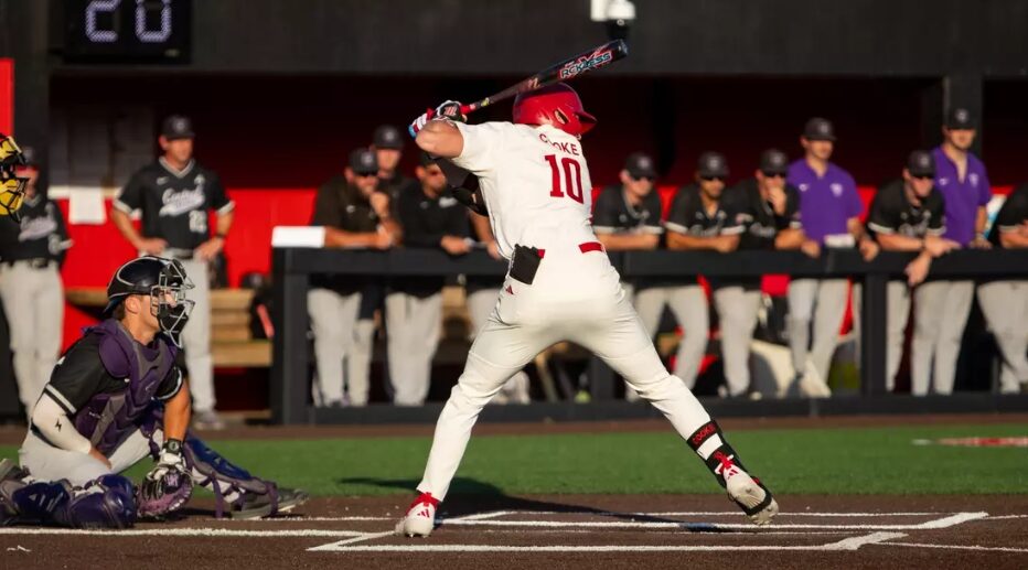 Baseball batter in a white uniform with number 10 swings at a pitch near home plate, catcher crouched behind him.