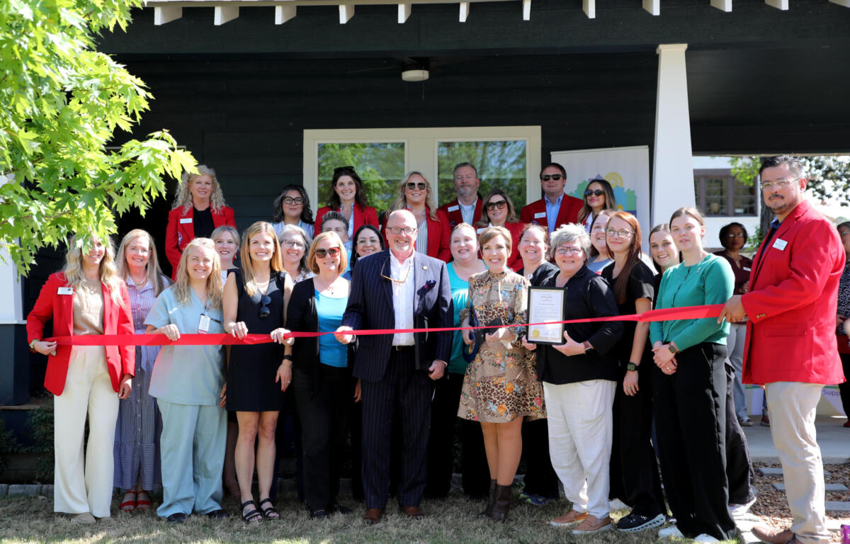 Group of people at a ribbon-cutting ceremony in front of a dark building, many wearing red blazers and name tags.