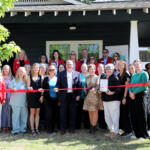 Group of people at a ribbon-cutting ceremony in front of a dark building, many wearing red blazers and name tags.