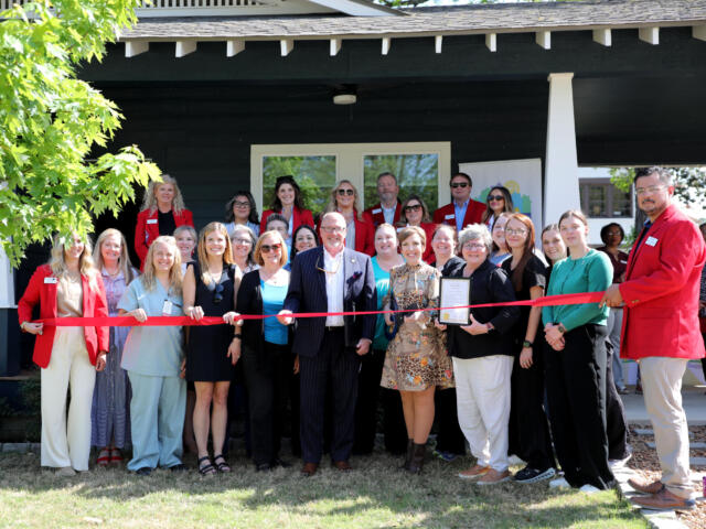 Group of people at a ribbon-cutting ceremony in front of a dark building, many wearing red blazers and name tags.
