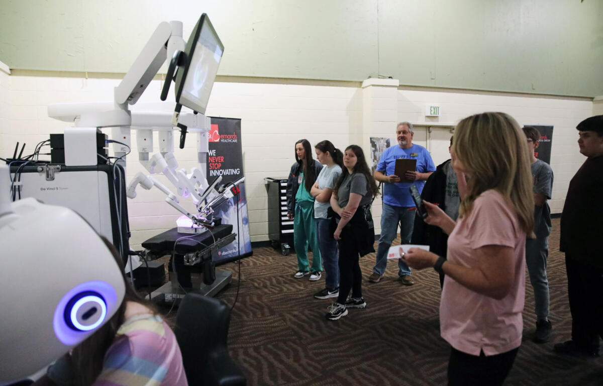 Group of people watching a row of white robotic arms on display in a science/tech booth.