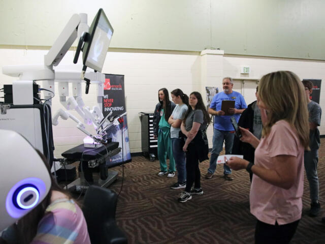 Group of people watching a row of white robotic arms on display in a science/tech booth.