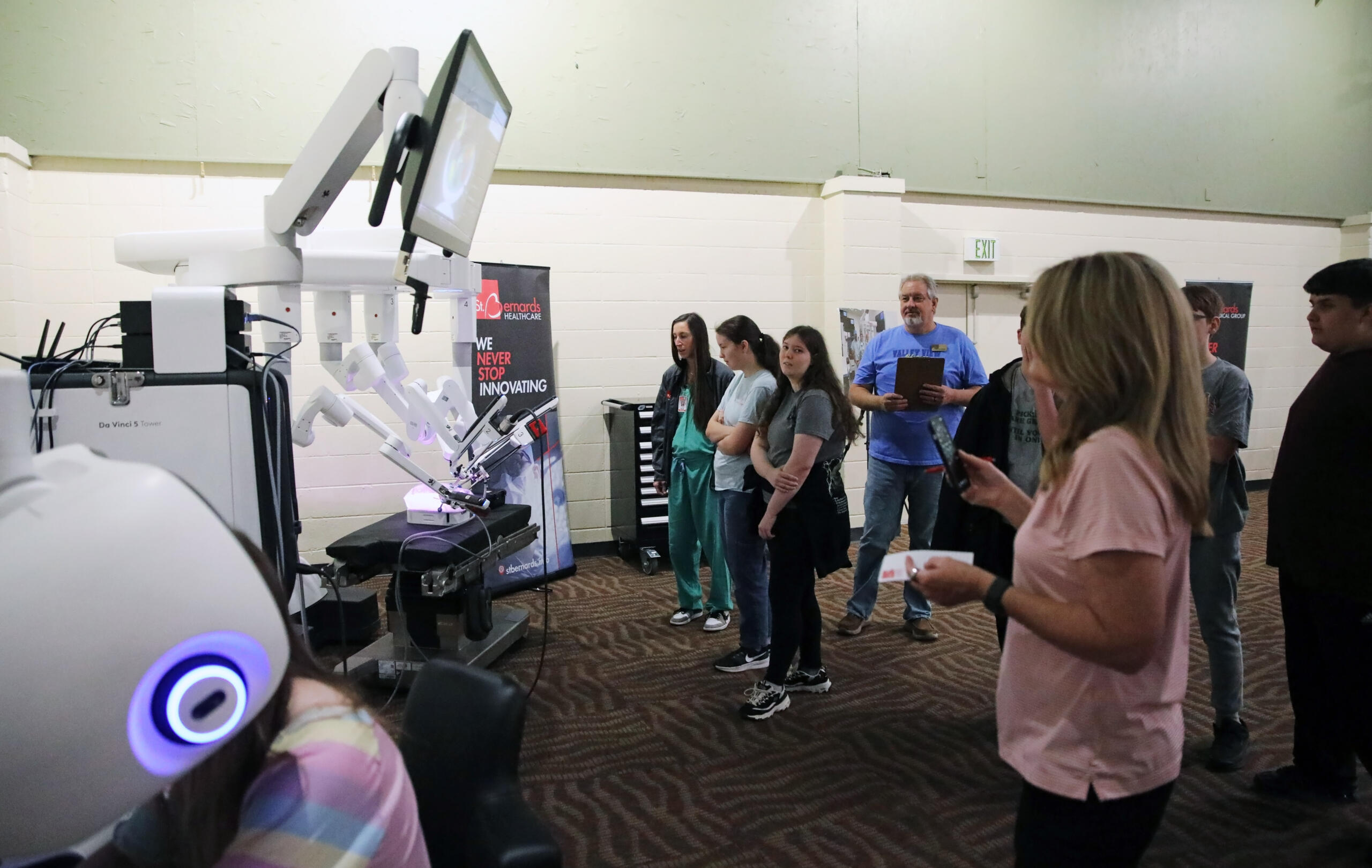 Group of people watching a row of white robotic arms on display in a science/tech booth.