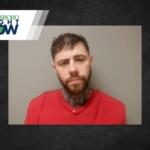 Mugshot-style photo of a man with a beard in a red shirt, facing the camera against a gray wall; a Jonesboro Right Now logo/banner overlaps the top-left corner.