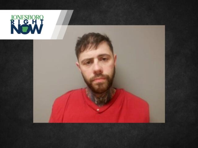 Mugshot-style photo of a man with a beard in a red shirt, facing the camera against a gray wall; a Jonesboro Right Now logo/banner overlaps the top-left corner.