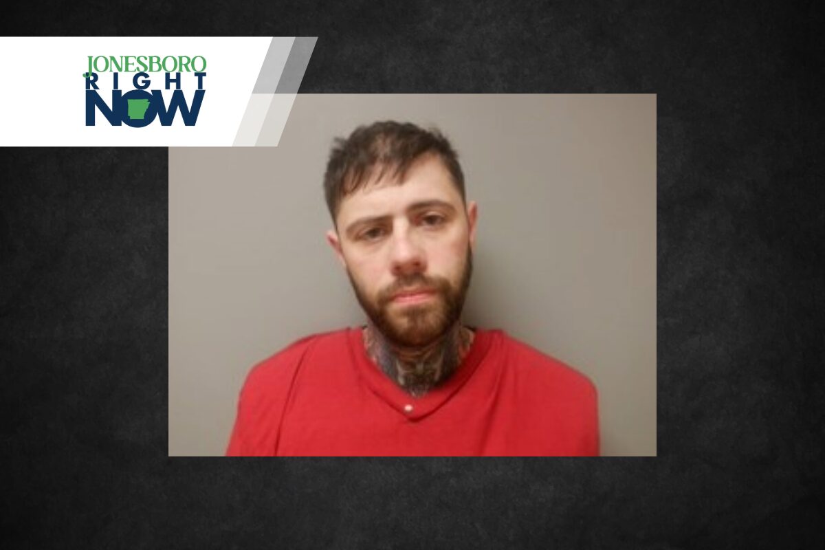 Mugshot-style photo of a man with a beard in a red shirt, facing the camera against a gray wall; a Jonesboro Right Now logo/banner overlaps the top-left corner.
