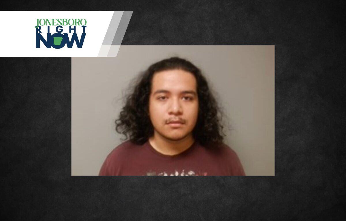 Mugshot of a young man with shoulder-length curly hair in a maroon shirt, gray backdrop, with a Jonesboro Right Now banner at top-left.