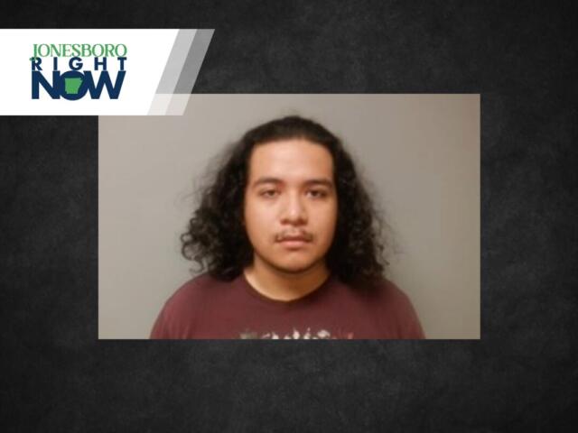 Mugshot of a young man with shoulder-length curly hair in a maroon shirt, gray backdrop, with a Jonesboro Right Now banner at top-left.