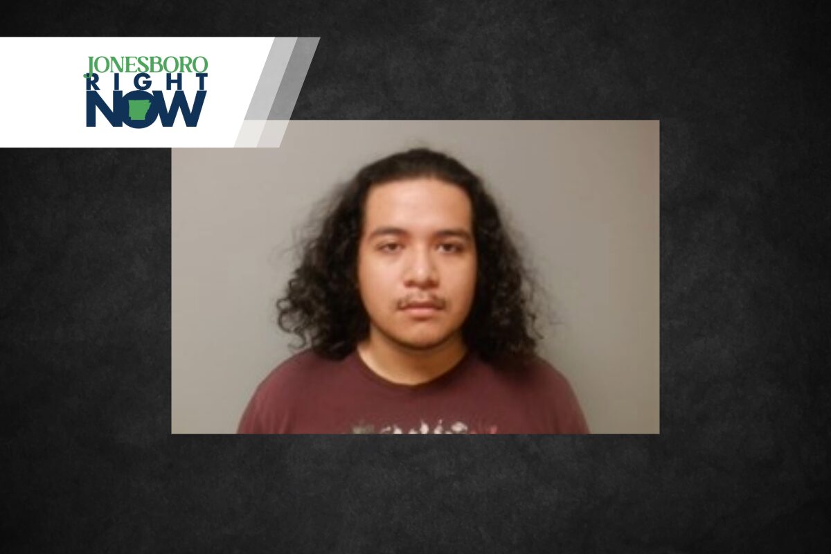 Mugshot of a young man with shoulder-length curly hair in a maroon shirt, gray backdrop, with a Jonesboro Right Now banner at top-left.