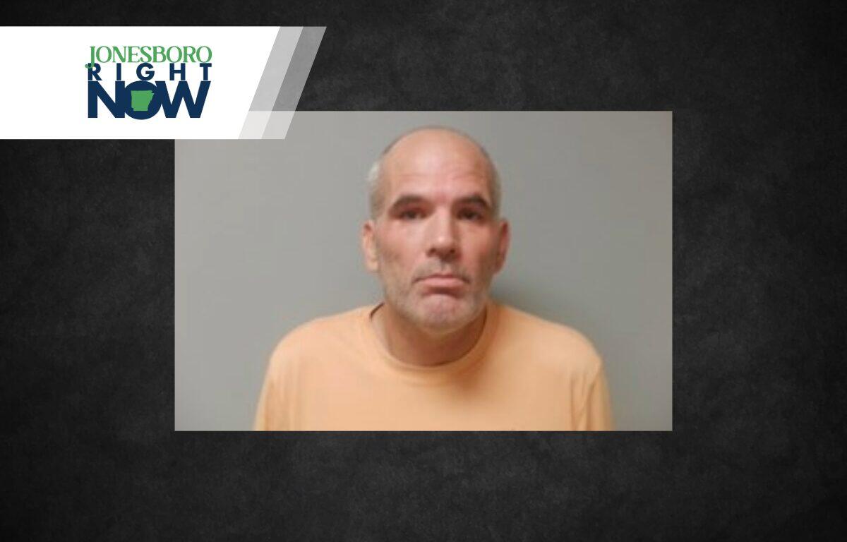 Mugshot of a middle-aged man with gray beard and short hair wearing an orange shirt against a gray backdrop.
