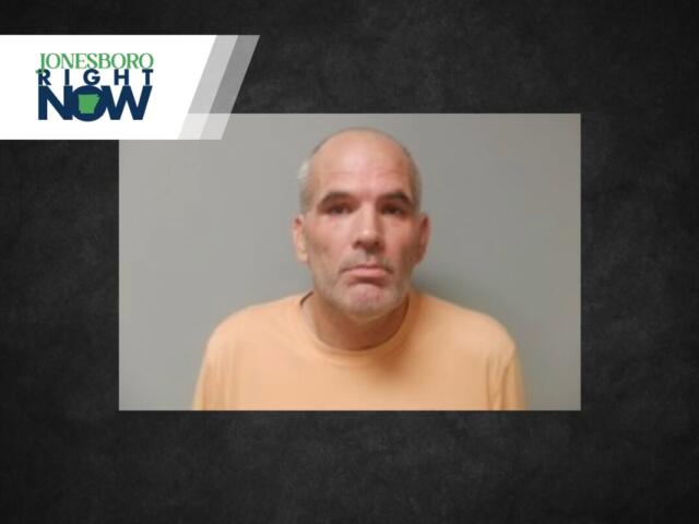 Mugshot of a middle-aged man with gray beard and short hair wearing an orange shirt against a gray backdrop.