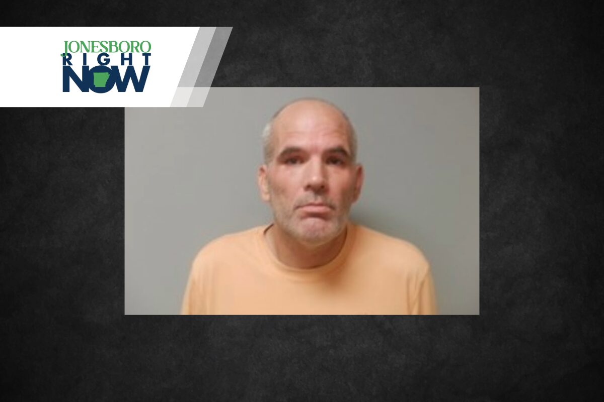 Mugshot of a middle-aged man with gray beard and short hair wearing an orange shirt against a gray backdrop.