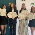 Six students in smart attire proudly display certificates at an ATU event with a branded backdrop behind them.