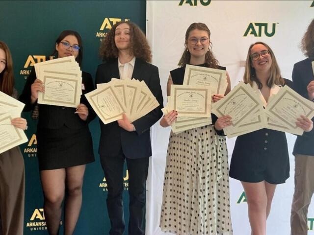 Six students in smart attire proudly display certificates at an ATU event with a branded backdrop behind them.