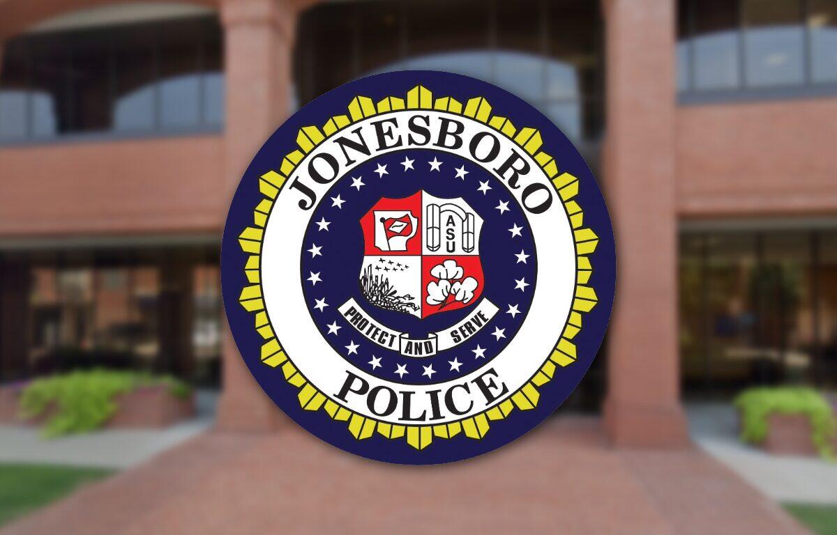 Circular Jonesboro Police Department seal with a yellow outer border, displayed on a brick building entrance in the background.