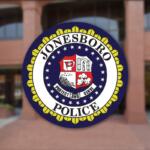 Circular Jonesboro Police Department seal with a yellow outer border, displayed on a brick building entrance in the background.