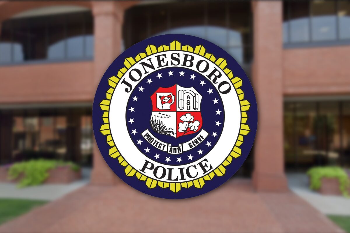 Circular Jonesboro Police Department seal with a yellow outer border, displayed on a brick building entrance in the background.