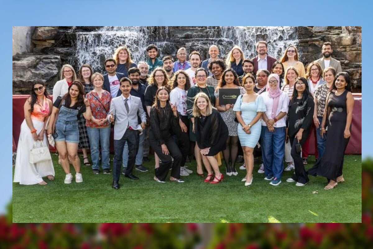 Diverse group of people posing for a group photo on a grassy outdoor area with a waterfall backdrop behind them.