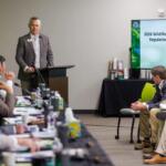 man in gray suit presents before room of people
