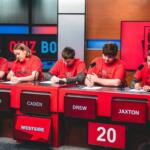 Five students in red shirts sit at a quiz bowl panel with microphones; nameplates read AVAH, CADEN, DREW, JAXTON; score 20 on a red panel.