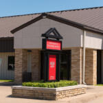 Entrance to Information & Technology Services at a campus building with a red sign in a black frame, beige brick columns and a raised garden bed in front.
