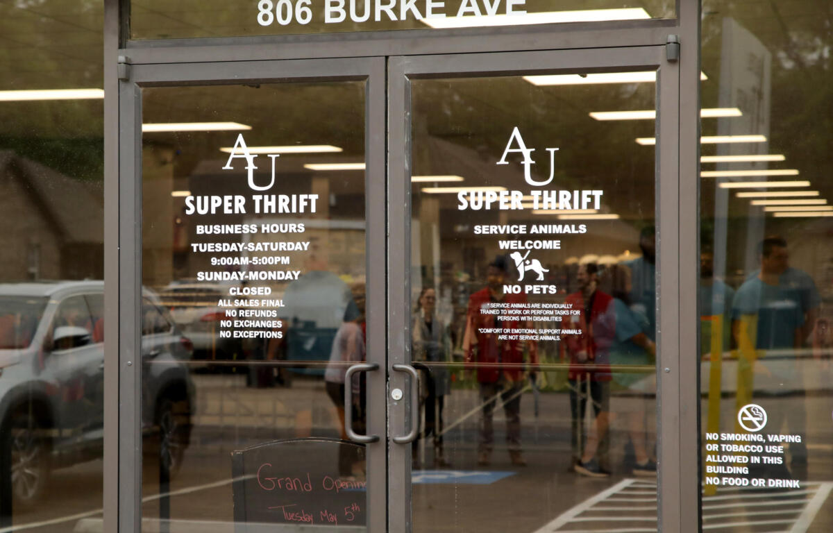Storefront glass doors with '806 BURKE AVE' sign; doors show 'SUPER THRIFT' logo and store policies like no pets and no smoking (reflections visible).