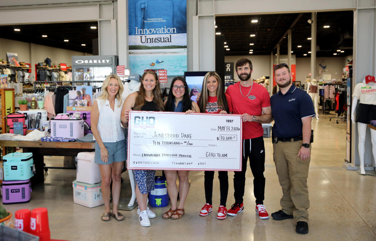Six smiling people in a sporting goods store pose with a giant $10,000 check.