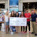 Six smiling people in a sporting goods store pose with a giant $10,000 check.