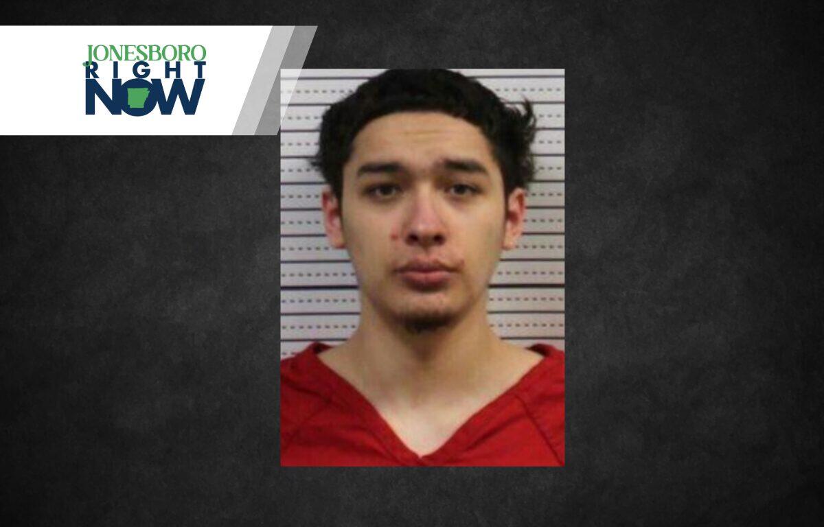 Mugshot of a young man with dark hair wearing a red shirt, posed against a measurement background; Jonesboro Right Now logo in the top-left corner.