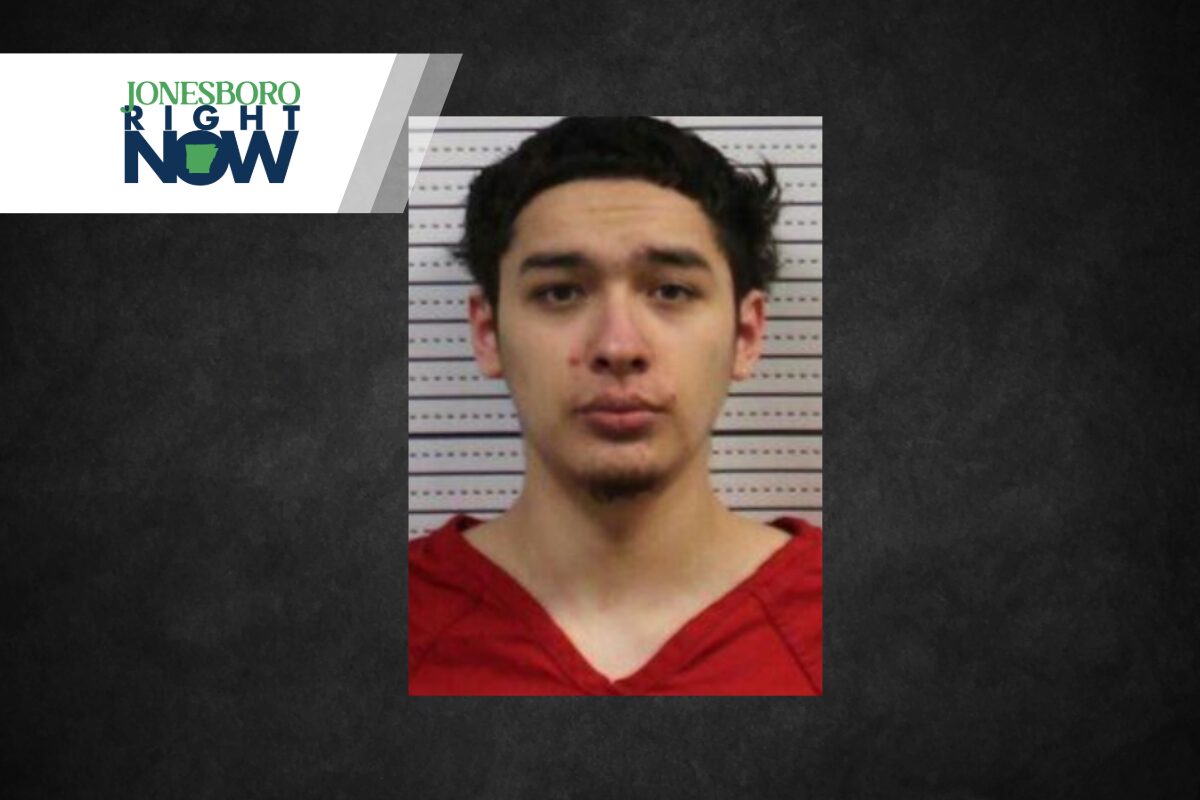 Mugshot of a young man with dark hair wearing a red shirt, posed against a measurement background; Jonesboro Right Now logo in the top-left corner.