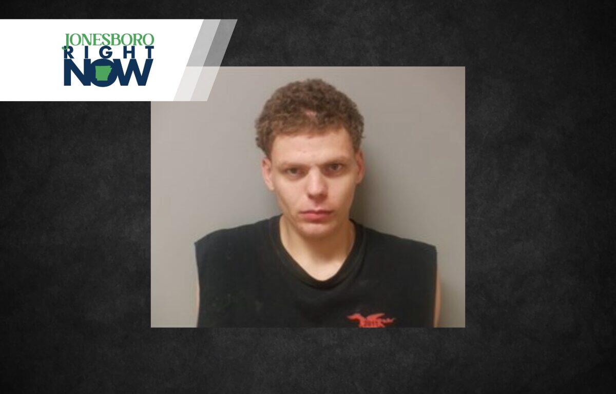 Mugshot of a young man with short curly hair in a black sleeveless shirt against a gray wall, with a Jonesboro Right Now logo in the top-left corner.